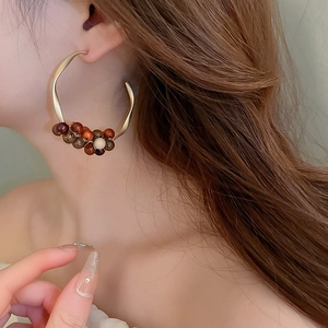 Close-up of model wearing large C-shaped metal earrings with colorful wooden beads