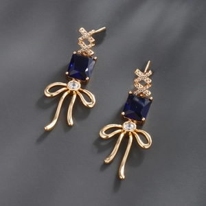 Macro detail of gold earrings with blue square gemstone and zircon bow accents