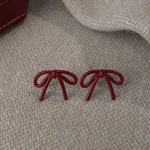 Detail view of deep red bow stud earrings with 2.2cm size measurement on knit fabric