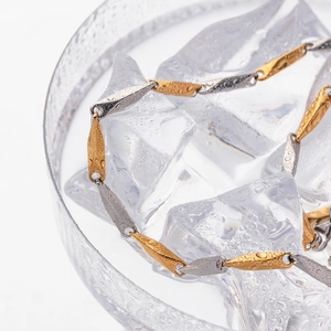 Detailed macro view of faceted gold and silver chain links with water droplets on ice