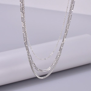 Detail of a silver-toned three-layer necklace with cable, rectangle and box chain links