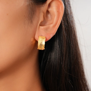 Close-up of 18K gold plated hoop earring with textured stripe surface on model's ear