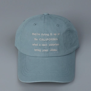 Detail of blue cotton baseball cap featuring white embroidered lyrics and reinforced brim