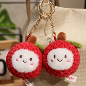 Cute plush lychee keychain set in vibrant red with smiling faces hanging on a beige bag