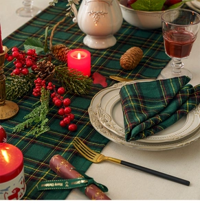 Close-up of green plaid table runner with festive red candles and pine cone decor