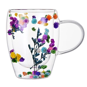 Double-walled glass mug with dried flowers inside and ergonomic handle on white background