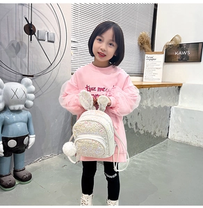 Close-up of white sequined toddler backpack with 3D bunny ears and fuzzy pom pom detail