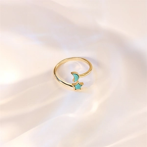 Close-up of golden open ring with turquoise star and moon on pearl fabric