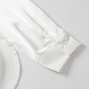 Détail de la manche d'une chemise en satin blanc avec bouton et texture de tissu lisse