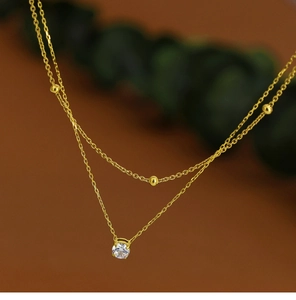 Close-up of double layer gold necklace featuring small beads and a clear zircon pendant