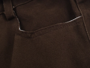 Dettaglio del tessuto denim twill marrone scuro con cuciture rinforzate sulla tasca