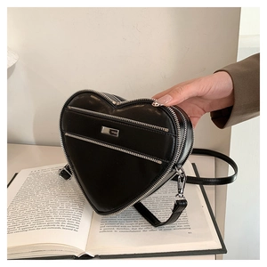 Detail shot of heart-shaped black leather bag with decorative silver zippers on a book