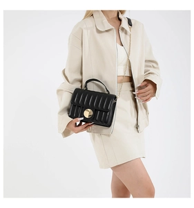 Close-up of black quilted shoulder bag with gold round buckle on beige outfit