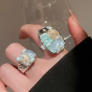 Detail of silver rings featuring seashells, light blue gems and pearls on a model's hand