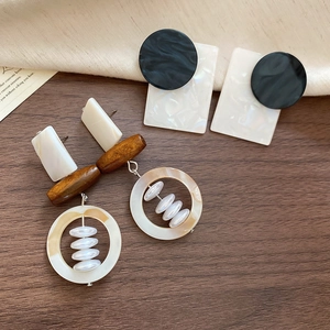 Flat lay of vintage square shell and wooden bead geometric earrings on textured fabric