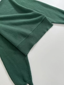Close-up of the ribbed hem and cuff detail on this dark green knit sweater top