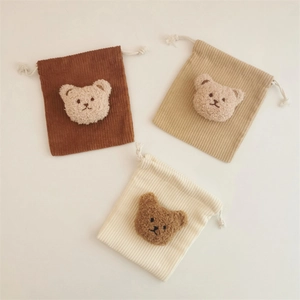 Detail of three corduroy drawstring bags in brown beige and white with plush bear patches
