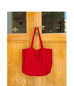 Close-up of red corduroy tote bag texture and front pocket on a wooden door handle