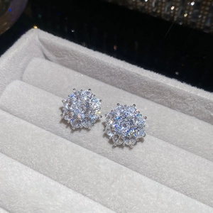 Detail view of sparkling zircon flower ear clips resting on a grey velvet jewelry box padding