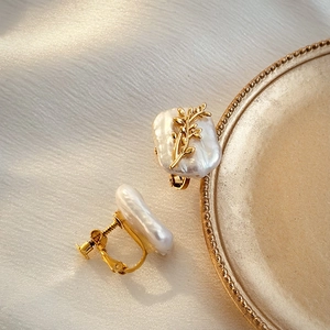 Detail of baroque pearl ear clips with golden leaf accents on elegant white fabric