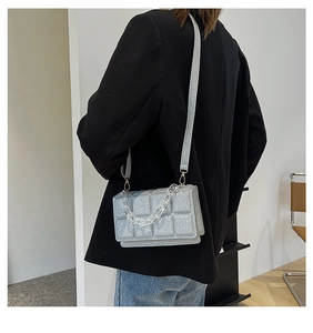 Detail of silver glitter crossbody bag with quilted pattern and acrylic chain on model