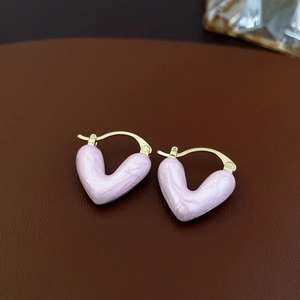 Détail de boucles d'oreilles cœur en marbre rose avec dorure sur un fond de cuir marron