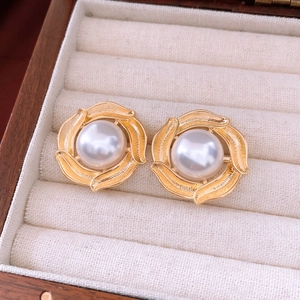 Macro detail of golden twist earrings with white pearl center set in a velvet jewelry box