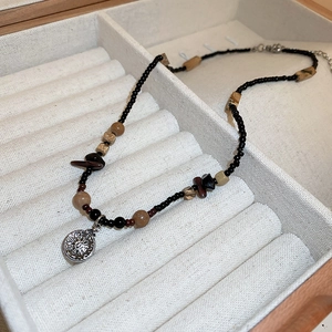 Detail of handcrafted beaded necklace with circular metal pendant in a beige jewelry box