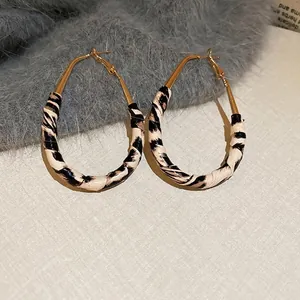 Close-up of golden teardrop earrings with retro leopard print patterns on a plush surface