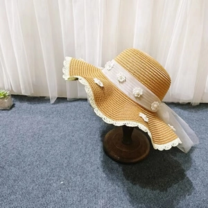 Detail eines Strohhutes mit weißem Spitzenbesatz, 3D-Blumen und einem transparenten Band
