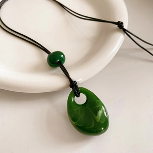Macro shot of green teardrop resin pendant on black wax cord over a white ceramic dish