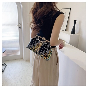 Black sequined evening clutch bag with metal chain strap shown on model shoulder