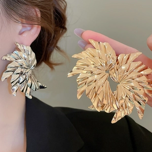 Detail showing oversized metallic spiral fan earrings with pleated texture in gold and silver