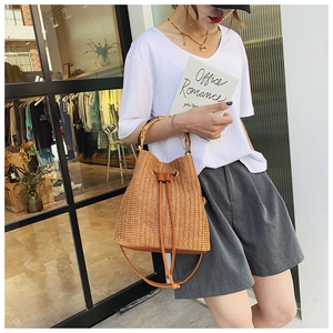 Detail of woven straw bucket bag featuring a natural bamboo handle and leather drawstring
