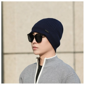 Close-up of deep blue ribbed knit beanie with decorative side label on model outdoors