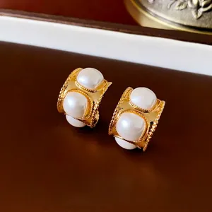Vintage C-shaped gold earrings with four white pearls on a textured brown leather backdrop