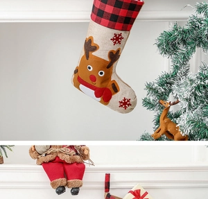 Detail of burlap Christmas stocking with reindeer pattern and red plaid cuff on a fireplace