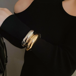 Detail of high-polish gold and silver wide cuffs worn over black knit sleeve style
