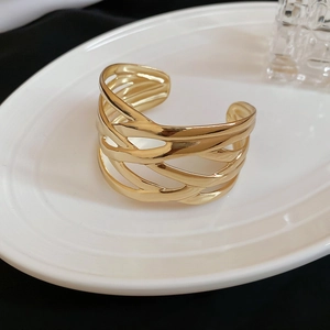 Detailed view of the gold open cuff bracelet with woven texture on a white ceramic plate