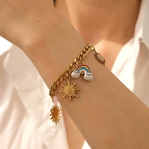 Close-up of gold stainless steel bracelet featuring sun and rainbow charms on a wrist