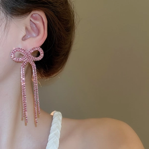 Macro detail of sparkling pink bow earrings with rhinestone tassels worn by a model