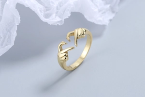 Detailed close-up of golden metal ring featuring a unique heart gesture hand design