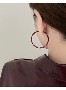 Detail of twisted burgundy round hoop earrings with glossy geometric texture on model
