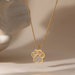 Close-up of golden paw print necklace with white zircon stones on a ball chain