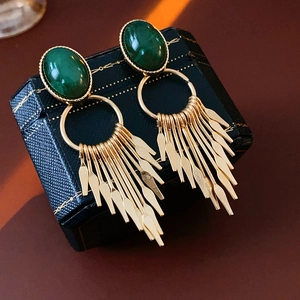 Detailed macro of vintage style earrings with green gemstones and gold tassel pendant
