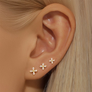 Close-up of three gold stud earrings with white zircon on ear model including flower designs