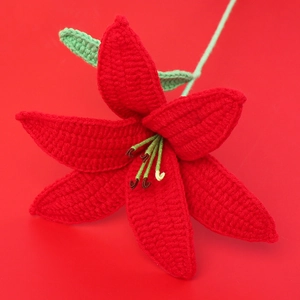 Close-up of a handmade red crochet lily flower with green leaves on a matching red background