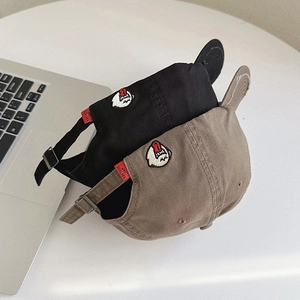Close-up of black and khaki baseball caps with red woven tags and ghost embroidery
