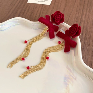 Detailed close-up of velvet rose and bow earrings with long golden tassels and red beads