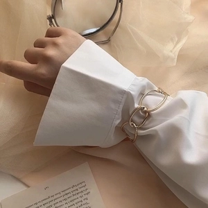 Detailed view of a gold chain link bracelet worn over a white shirt sleeve
